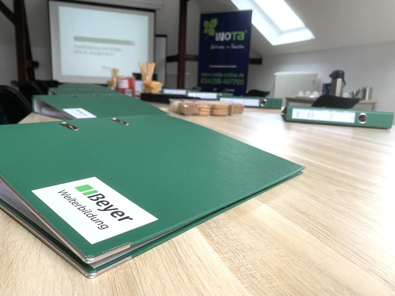 Schulung mit 7 Teilnehmenden, die vor einer Leinwand sitzen und der Schulungsleitung zuhören